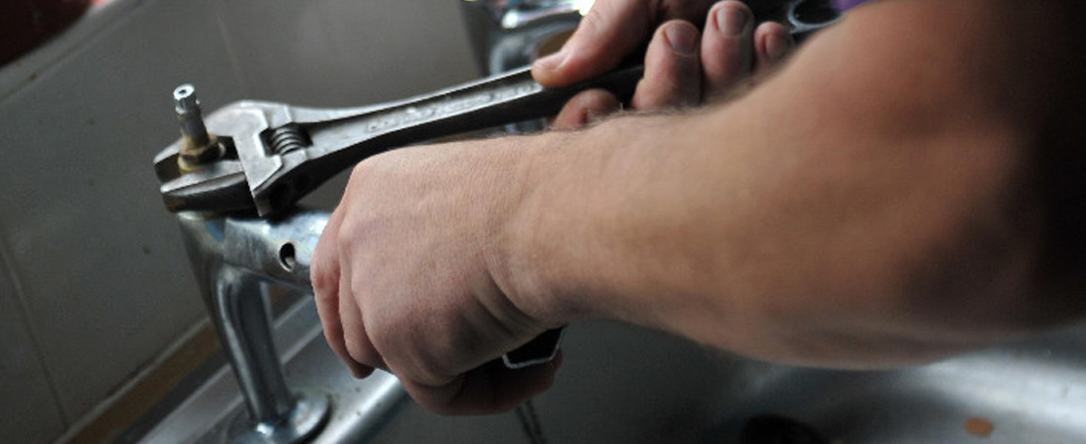 A close up of hands holding a wrench fixing taps