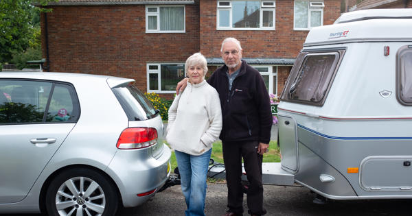 Elderly Couple Standing Outside Of Cars And Home