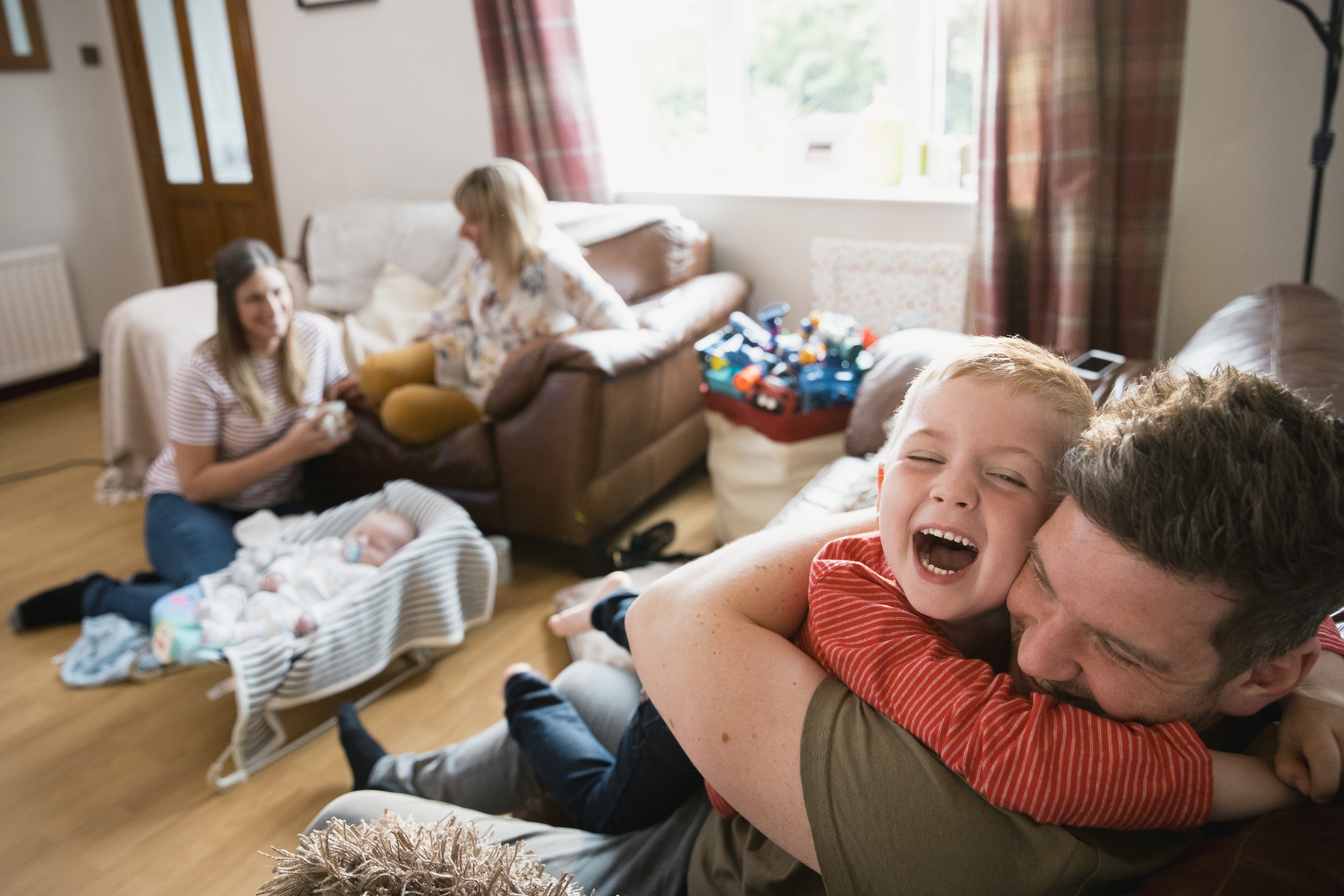 Father and child cuddle on the sofa as two women sit on the floor further away