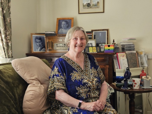 An elderly women sitting on a chair, wearing a blue dress.