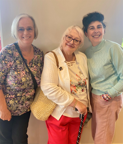 Three women standing of varying ages standing in front of a plain white wall