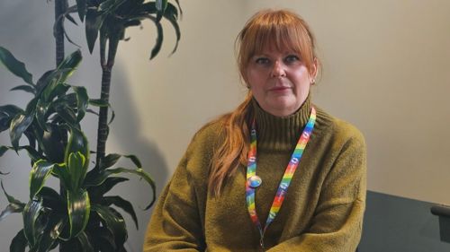 A women wearing a green jumper, she has red hair and is looking serious.