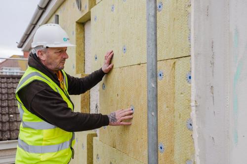 Man fitting insulation to the outside of a building