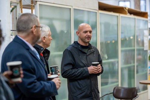 A man holding a coffee cup talking to a group of people.