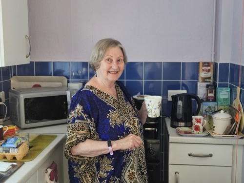Elderly women in the a purple kitchen drinking a tea.