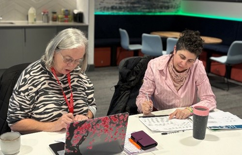 Two women sitting around a table looking at paper.