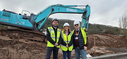 Three people wearing hi viz in front of a digger