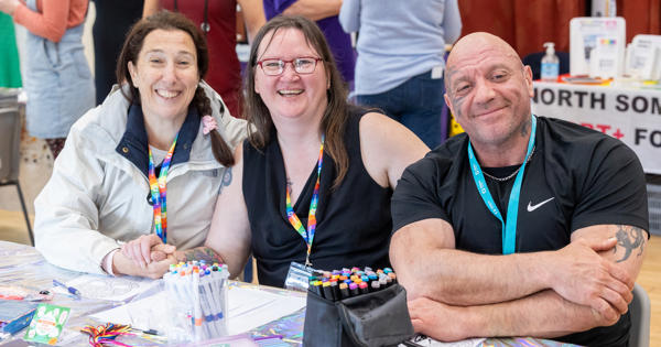 Two women and a man smiling behind a table with pens