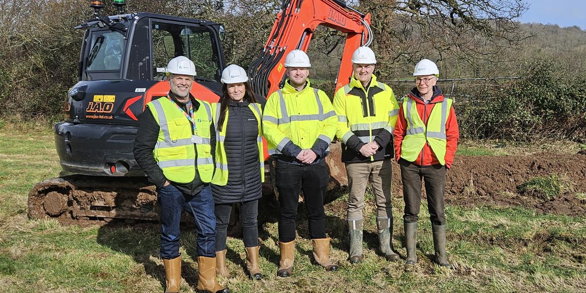 5 people in a field wearing hi viz in front of a digger