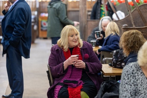 A women wearing a purple coat and red scarf talking to an Alliance Homes colleague.