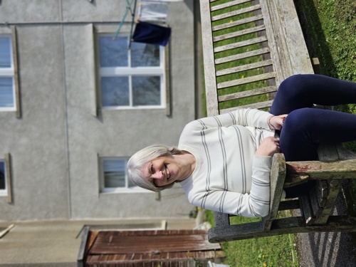 Woman sitting outside on a wooden bench against a grey building.